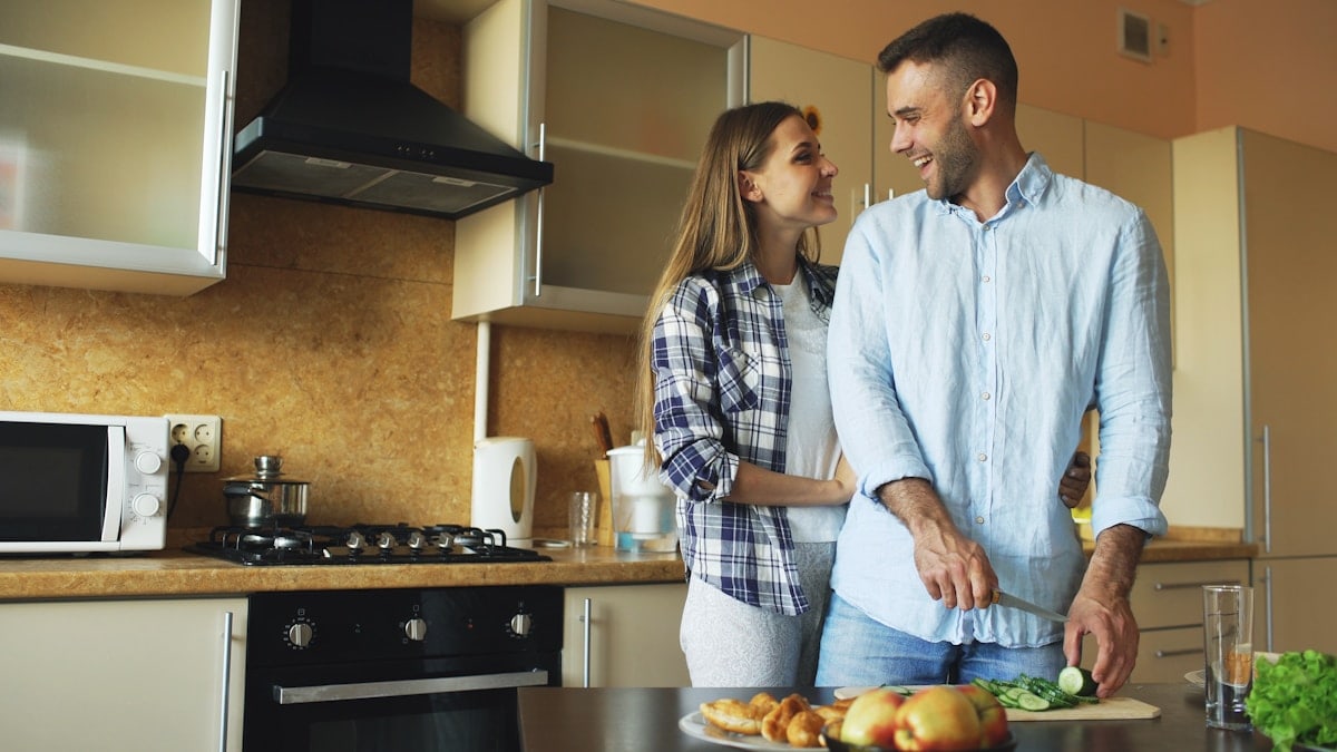 Happy young couple embracing and talking in the kitchen while cooking breakfast at home in the morning