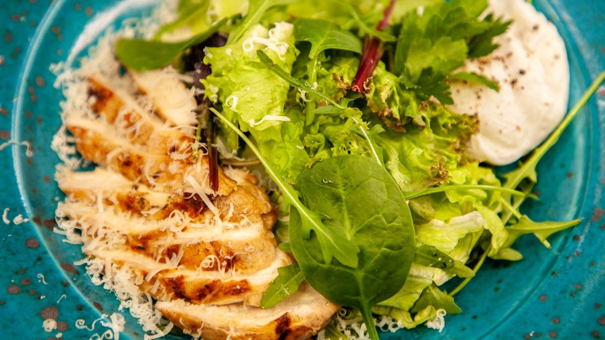 Close-up of a grilled chicken salad with mixed greens and cheese, served on a blue plate.